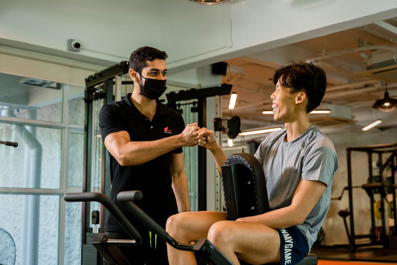 A personal trainer fist bumps a smiling client, promoting fitness motivation in a Singapore gym.